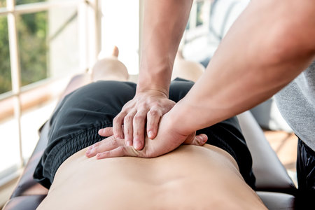 Therapist giving lower back sports massage to athlete male patient in clinic