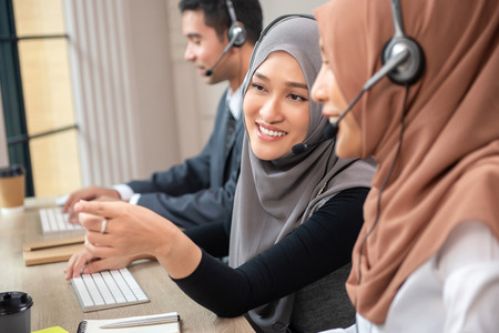 Happy beautiful Asian muslim women working in call center office together with colleaguesの写真素材