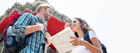 Young tourist couple backpackers traveling in ancient Thai temple on summer vacations in Bangkok Thailand, panoramic banner with copy spaceの写真素材
