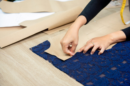 Designer hands pinning paper pattern on fabric at the table making dress in tailor shopの写真素材