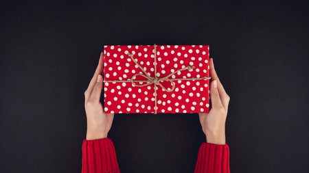 Woman hands giving red christsmas gift box top view on black background