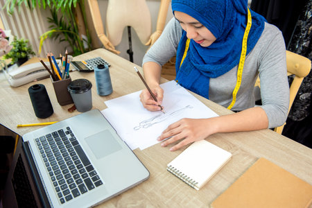 Muslim woman fashion designer drawing a dress design sketch in paper at the table