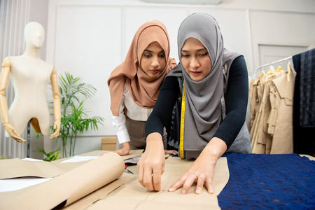 Muslim woman fashion designer pinning paper pattern on fabric at the table in tailor shopの写真素材