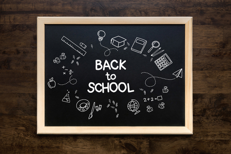 Square framed blackboard with doodles and back to school text over a wooden table backgroundの写真素材