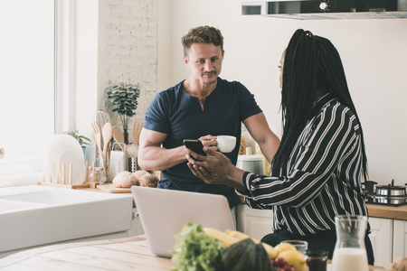African American wife showing information on mobile phone to her husband during breakfast time at home in kitchenの写真素材