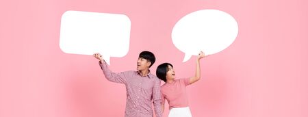 Happy smiling young Asian couple with speech bubbles studio shot on pink banner backroundの写真素材