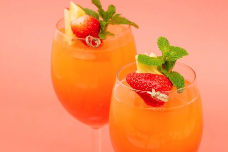 Closeup shot of colorful refreshing strawberry orange sunrise cocktail drinks in the glasses on coral pink backgroundの写真素材
