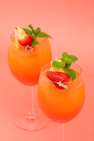 Colorful refreshing strawberry orange sunrise cocktail drinks in the glasses on coral pink backgroundの写真素材