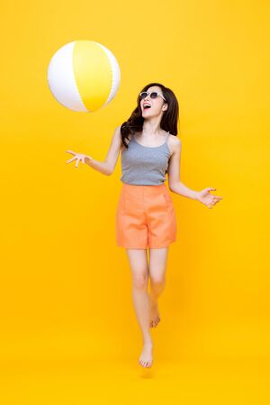 Happy young Asian woman in casual summer clothes playing beach ball in colorful yellow backgroundの写真素材