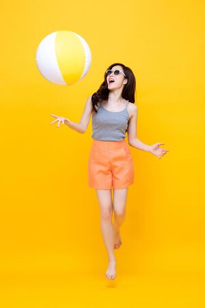 Happy young Asian woman in casual summer clothes playing beach ball in colorful yellow background