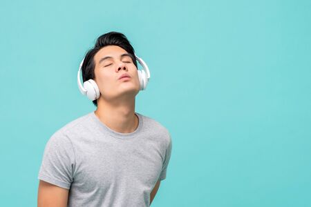 Happy young Asian man enjoying listening to music with headphones studio shot isolated on light blue background with copy spaceの写真素材
