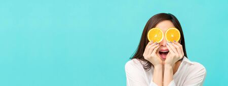 Young woman with fresh sliced oranges at the eyes isolated on light blue banner background with copy spaceの写真素材