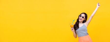 Happy Asian woman in summer casual clothes with fresh fruit juice drink isolated on colorful yellow banner background with copy spaceの写真素材