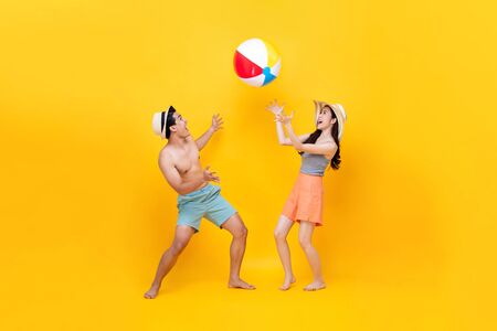 Happy fun Asian couple playing beach ball together in colorful yellow backgroundの写真素材