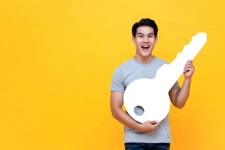 Excited young Asian man holding big mockup car key studio shot in yellow background with copy space