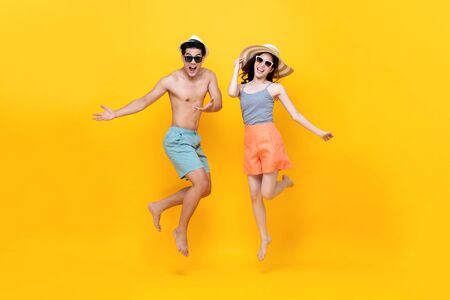 Playful energetic Asian couple in summer beach casual clothes jumping on yellow background studio shotの写真素材
