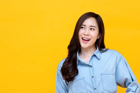 Smiling Asian woman in casual shirt looking at copy space aside studio shot isolated on colorful yellow backgroundの写真素材
