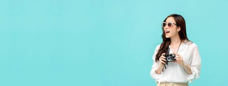 Young amazed asian woman tourist photographer in casual attire holding a camera in light blue banner background with copy spaceの写真素材