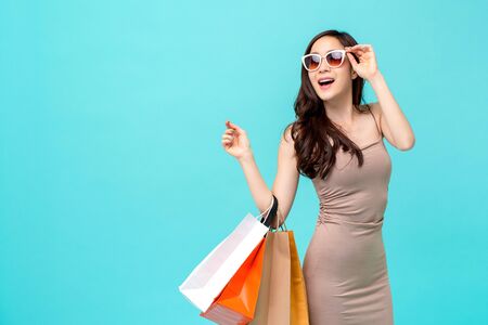 Happy beautiful Asian shopaholic woman carrying shopping bags in colorful light blue background with copy space for summer sale conceptの写真素材