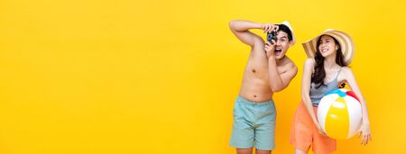 Lovely Asian couple in summer casual clothes with beach accessories isolated on colorful yellow banner background with copy spaceの写真素材