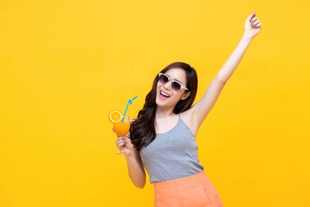 Happy Asian woman in summer casual clothes with a glass of fresh fruit juice drink studio shot isolated on colorful yellow backgroundの写真素材