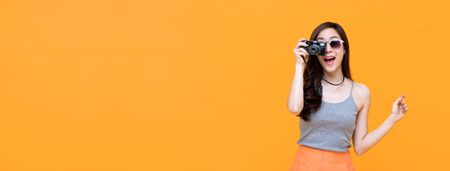 Young amazed asian woman tourist in casual clothes taking a photo on a yellow banner background with copy spaceの写真素材