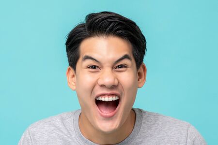 Closeup shot of delighted excited Asian man face isolated on light blue backgroundの写真素材