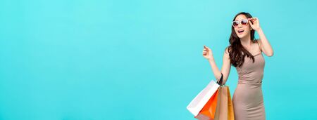 Happy beautiful Asian shopaholic woman carrying shopping bags in colorful light blue banner background with copy space for summer sale conceptの写真素材