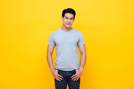 Handsome young Asian man in plain light gray t-shirt studio shot isolated on colorful yellow backgroundの写真素材