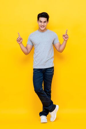 Happy smiling young handnsome Asian man pointing hands up to empty space asideの写真素材
