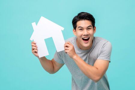 Portrait of young handsome happy Asian man holding paper home for real estate conceptの写真素材