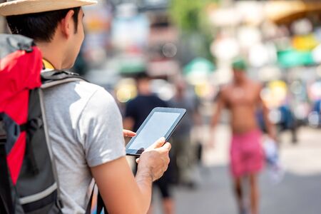 Male tourist backpacker using tablet computer searching for location while traveling on vacations in Khao San road Bangkok Thailandの写真素材