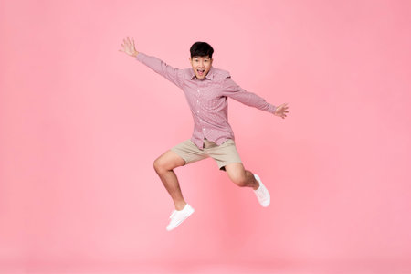 Energetic happy smiling young Asian man in casual clothes jumping studio shot isolated in colorful...