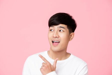Smiling young handsome Asian man pointing hand to empty space asideの写真素材