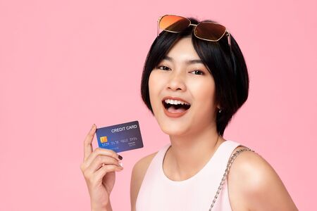 Young pretty Asian woman with credit card in hand studio shot isolated on colorful pink backgroundの写真素材