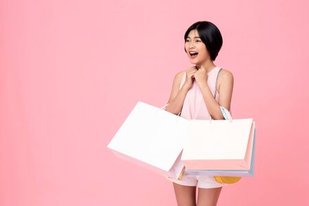 Young Asian woman carrying shopping bags in surprised and excited gesture studio shot isolated on pink background with copy spaceの写真素材