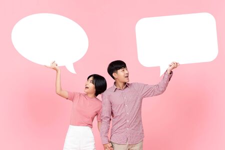 Lovely smiling young Asian couple with speech bubbles studio shot on pink backgroundの写真素材