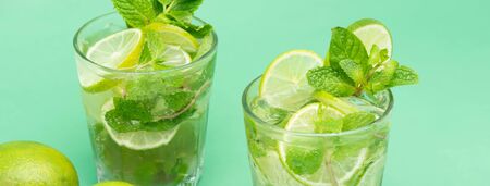 Refreshing Mojito cocktail drinks in the glasses with fresh sliced limes and peppermint leaves on green banner backgroundの写真素材