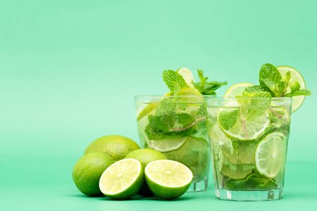 Refreshing Mojito cocktail drinks in the glasses with fresh sliced limes and peppermint leaves on green backgroundの写真素材