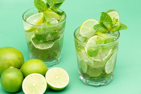 Refreshing Mojito cocktail drinks in the glasses with fresh sliced limes and peppermint leaves on green backgroundの写真素材