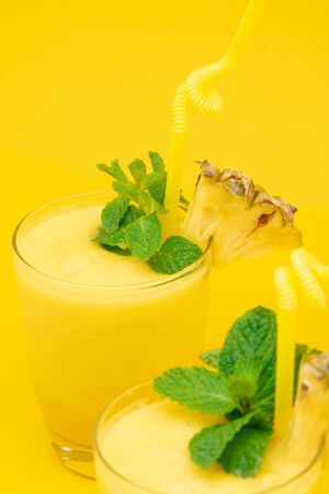 Refreshing healthy pineapple smoothie drinks in the glasses garnished with peppermint on yellow backgroundの写真素材