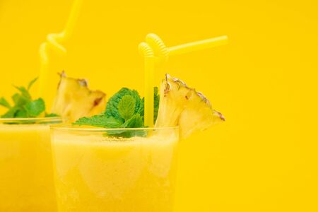 Refreshing healthy pineapple smoothie drinks in the glasses garnished with peppermint on yellow background with copy spaceの写真素材
