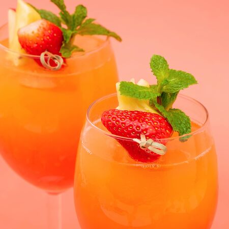 Closeup shot of colorful refreshing strawberry orange sunrise cocktail drinks in the glasses on coral pink backgroundの写真素材