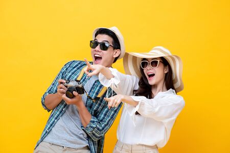 Happy excited young Asian couple tourists in colorful yellow background