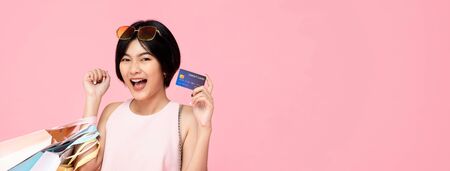 Young pretty Asian woman with shopping bags showing credit card in hand studio shot isolated on pink banner background with copy spaceの写真素材