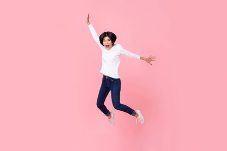 Studio shot of happy energetic asian woman wearing casual clothes jumping in mid-air motion isolated in pink backgroundの写真素材
