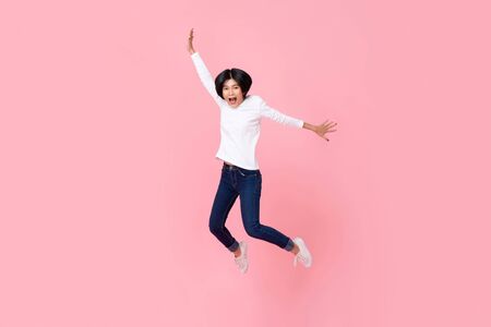 Studio shot of happy energetic asian woman wearing casual clothes jumping in mid-air motion isolated in pink background