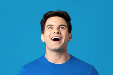 Young handsome delighted caucasian man looking up with mouth open isolated on light blue backgroundの写真素材