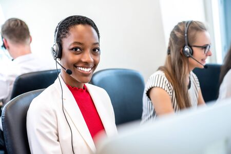 Smiling beautiful African American woman working in call center office with diverse team as the customer care operatorsの写真素材