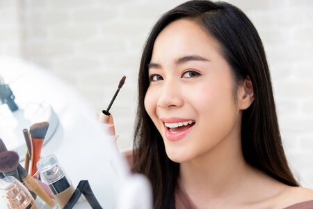 Young beautiful smiling Asian woman using mascara makeup for eyelashesの写真素材